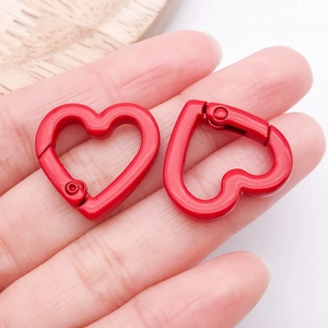 Detail of red heart-shaped alloy spring clasps for DIY bag charms on fingertips