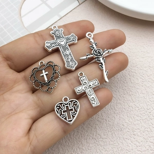 Cinq pendentifs vintage en argent avec cœurs et croix tenus en main sur un plateau