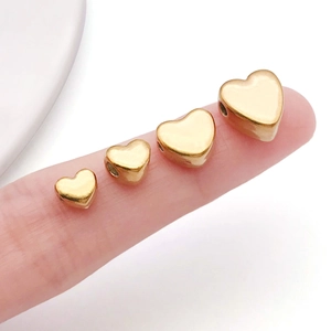 Detailed view of four golden heart-shaped spacer beads in varying sizes on a finger