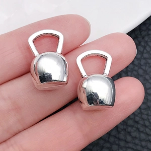 Macro view of silver miniature kettlebell charms held on fingertips for jewelry making