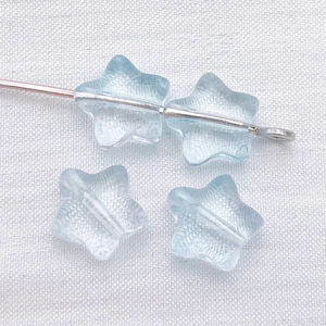Macro detail of 8mm light blue star-shaped glass spacer beads with translucent icy texture