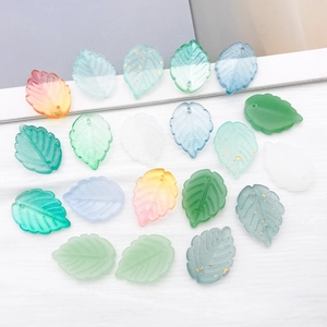 Detailed macro view of frosted glass leaf charms with gold foil inserts for DIY jewelry