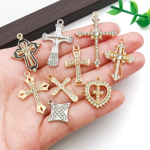 Assorted rhinestone cross pendants for jewelry making held by a hand on a clean background