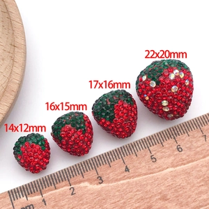 Macro view of strawberry resin charms in four sizes with red rhinestones and a ruler scale