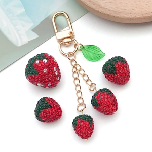 Golden keychain featuring 3D red rhinestone strawberry pendants and green leaves