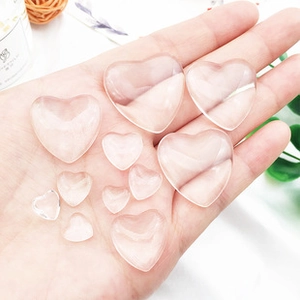 Transparent heart-shaped glass stones in multiple sizes shown in hand for scale