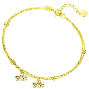 Detalle del dije 2023 en pulsera de doble cadena dorada con un pequeño colgante de corazón