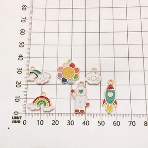 DIY colorful enamel charms featuring astronaut and rainbow designs on a grid background