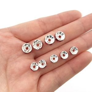 Silver spacer beads with red rhinestones for DIY bracelets held in a hand for scale