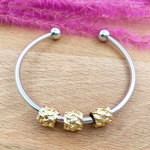 Detail of silver bangle featuring three golden woven beads on a light wood background