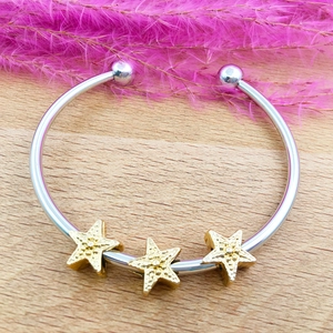 Detailed close-up of C-shaped silver bangle with golden star pendants and ball ends