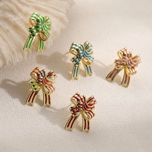 Macro shot of colorful enamel bow stud earrings on a textured white sand background