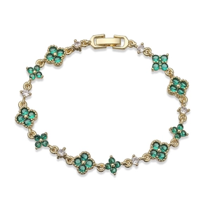 Detailed macro view of a gold clover bracelet with emerald green stones and pavé crystals
