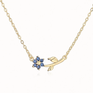Detail of gold necklace featuring a blue gemstone camellia flower pendant with leaves