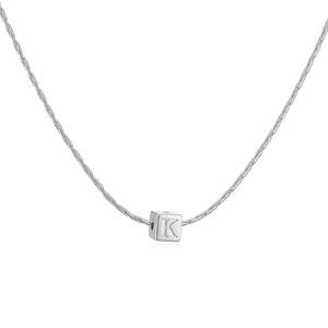 Détail macro d'une chaîne serpent argentée et d'un pendentif cube avec la lettre K