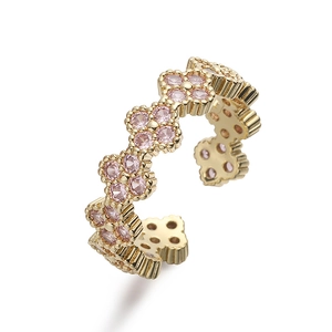 Detailed macro of gold four-leaf clover ring with pink crystals and textured band