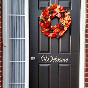 Autumn maple leaf wreath with pine cones and Welcome sign on a black front door