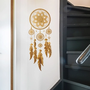 Décoration murale mandala dorée avec plumes en métal suspendues sur un mur blanc pur