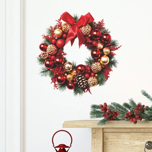 Christmas wreath with green pine needles, red ornaments, and a large red bow on a white wall