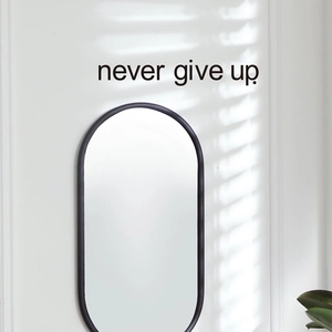 Miroir ovale noir moderne avec autocollant mural Never Give Up dans une chambre épurée
