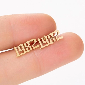 Macro shot of gold Gothic 1982 number earring held by hand to show compact size