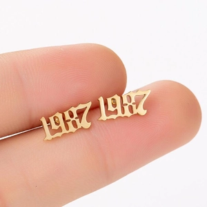 Detail of 1987 gothic number stud earring in gold finish held by hand for scale