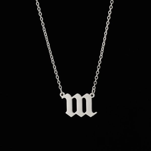 Detail of gothic silver letter m pendant with brushed metal texture on a fine chain