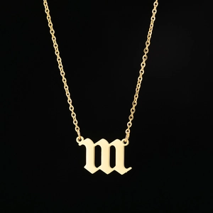 Macro detail of gothic letter m pendant in gold finish on a fine stainless steel chain