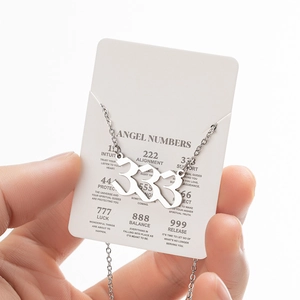 Close-up of silver angel number 333 pendant necklace on a branded display card