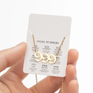 Detailed close-up of golden 999 angel number necklace on a white description card