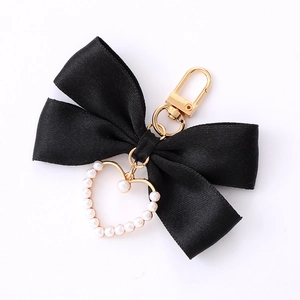 Elegant black bow keychain with pearl heart pendant and golden metal clip on white background