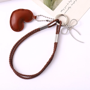Brown leather heart keychain with braided strap and silver bow charm on white background