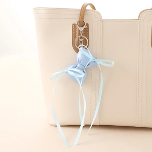 Sky blue satin ribbon bow bag charm with silver lobster clasp on a beige leather handbag