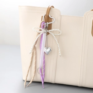 Nœud en perles et breloque cœur stylisés sur un sac à main en cuir blanc cassé