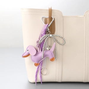 Purple dachshund bag charm with heart clasp on a white leather tote bag handle