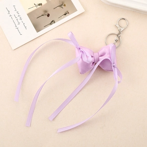 Detail of lavender satin ribbon bow keychain with silver metal rings on a beige surface