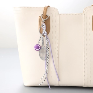 Tennis racket bag charm with purple plush ball and woven leather cord on a white tote