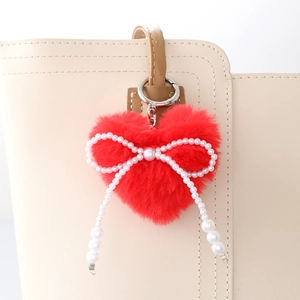 Porte-clés cœur en peluche rouge avec nœud en perles sur un sac à main en cuir beige