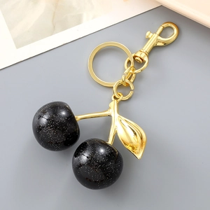 Macro detail of cherry bag charm featuring black glitter fruit and gold hardware