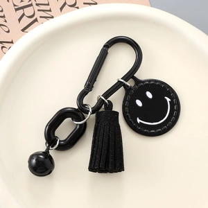 Black candy-colored smiley face keychain with metal links, tassel and bell on a plate