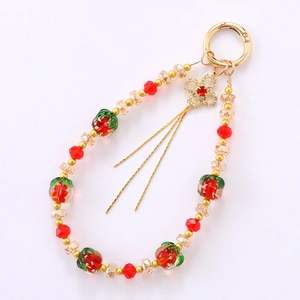 Beaded keychain wrist strap with red strawberry charm and golden clover tassel details