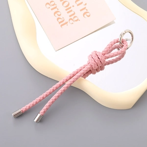 Handmade pink woven leather keychain with silver metal ring on a minimalist white tray