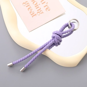 Detail of purple hand-woven leather keychain with silver metal ring on a modern tray