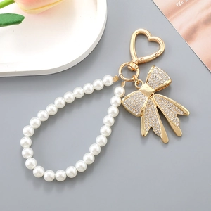 Porte-clés nœud en strass avec perles blanches et fermoir en cœur sur un fond gris doux
