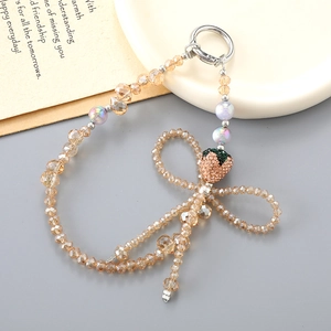 Détail d'une dragonne en perles de cristal champagne avec un pendentif fraise brillant