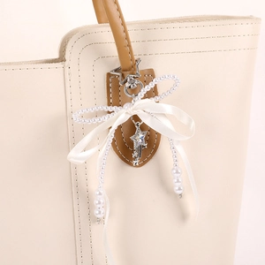 Sparkling star charm and white ribbon bow keychain accessory on beige leather handbag