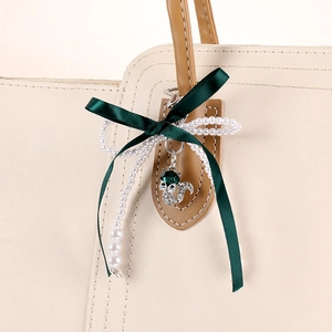 Green ribbon bow keychain with pearl beads and fox pendant hanging on a beige tote bag