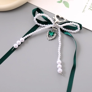 Détail de bijou de sac nœud vert foncé avec perles et pendentif papillon en cœur