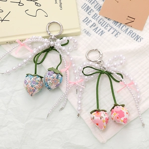 Handmade fabric strawberry bag charms with pearls and ribbon on a soft green background