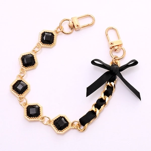 Golden aluminum bag chain with black gemstones and a silk ribbon bow accent